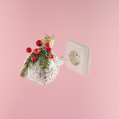 Christmas bauble with electrical outlet on pink background. Minimal New Year concept.