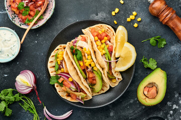 Mexican tacos with grilled chicken, avocado, corn kernels, tomato, onion, cilantro and salsa at black stone table. Traditional Mexican and Latin american street food. Top view.