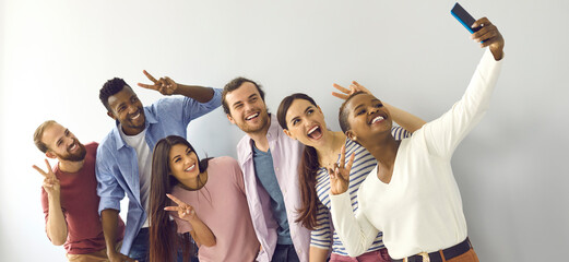 Happy cheerful laughing young adult diverse college student friends doing V sign hand gesture taking group phone selfie picture in studio, enjoying best time of life, making memories together. Header