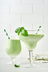 Detox green vegetable juice or smoothie garnished with leaf of fresh basil in coctail glass on light gray slate, stone or concrete background. Top view with copy space.