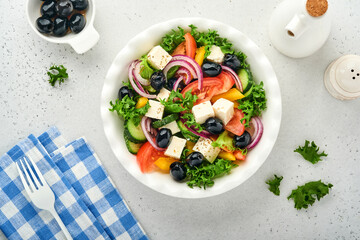 Traditional Greek salad of fresh cucumber, tomato, sweet pepper, lettuce, red onion, feta cheese and olives with olive oil on white plate. Healthy food, top view.