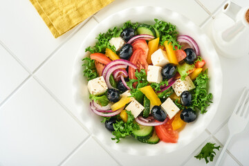 Traditional Greek salad of fresh cucumber, tomato, sweet pepper, lettuce, red onion, feta cheese and olives with olive oil on white plate. Healthy food, top view.
