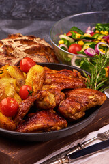 Fried chicken wings with potatoes on rustic background.