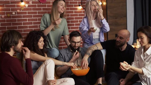 Friends grabbing popcorn from a bowl while sitting on a sofa at home