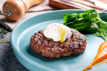 Minced beef steak with poached egg. Steak dish on a blue plate with spinach and pumpkin