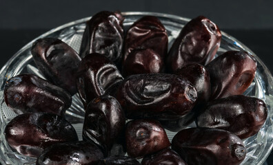 Crystal saucer with a bunch of dried dates on a dark background.