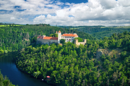 Old Moravian castle, standing on a rock promontory above the river Dyje against a summer blue sky with white clouds, surrounded by green forest. Tourist area. Aerial view of Bítov castle, Czechia.