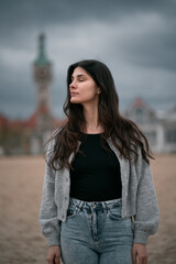 Sensual and gorgeous brunette on the beach. Clothed woman on the beach during autumn season on the seaside. Portrait of girl with brown hair wearing black shirt and jeans.