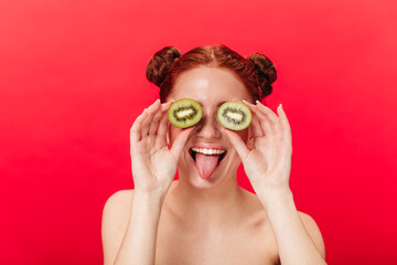 Studio shot of smiling girl with kiwi isolated on red background. Amazing young woman holding exotic fruits.