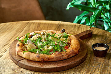Vegetarian wood-fired pizza with arugula, vegetables and parmesan on wood board. Selective focus