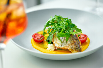 Fried sea bass fillet with arugula, tomatoes and yellow sauce in a gray plate. Selective focus