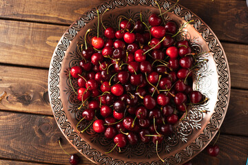 a lot of ripe cherries are lying on a copper tray with a pattern.