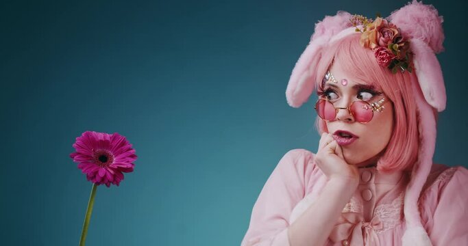 Pink sad cute candy anime girl in pink sunglasses someone makes a unexpected surprise flower gift and make her happy on blue background. Beautiful asian cosplay anime teen girl concept