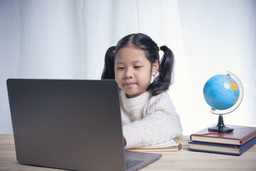 Asian kid girl writing follows teacher for learning an online lesson by video call the Internet...