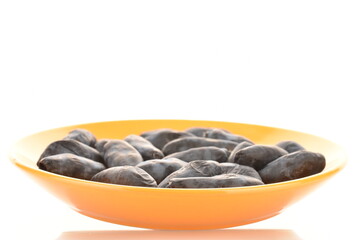 Several dark blue organic ripe honeysuckle berries on a yellow plate, close-up, isolated on white.