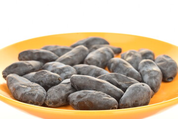 Several dark blue organic ripe honeysuckle berries on a yellow plate, close-up, isolated on white.