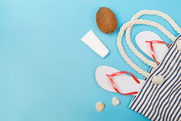 Top view photo of sunscreen, beach bag, flip flop, coconut on isolated blue background. Flat lay