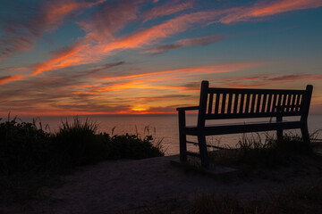 Obraz premium Sonnenuntergang an der Ostsee mit Sitzbank im Vordergrund