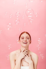 Obraz na płótnie Canvas Front view of joyful ginger woman with soap bubbles. Stunning caucasian girl laughing isolated on pink background.