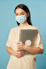 Young woman in protective mask standing and holding laptop