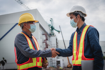 Two Asian workers shake hands at a construction site to suggest a start to hard work.