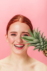 Front view of happy beautiful girl with pineapple. Studio shot of laughing ginger woman with tropical fruit.