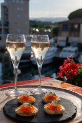 Russian style party with two glasses of white cold champagne, bliny with red caviar and view on Port Grimaud near Saint-Tropez in summer