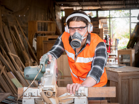Handsome Caucasian carpenter craftsman wearing safety gear working with hardwood using a miter saw to cut a piece of wood in the workshop. Manufacture of wood products. - Powered by Adobe