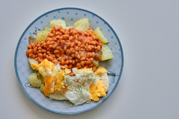 high angle view of a plate with potatoes beans in tomato sauce and fried eggs