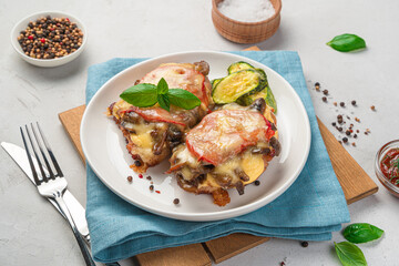 Baked meat with vegetables and cheese in a white plate on a gray background.