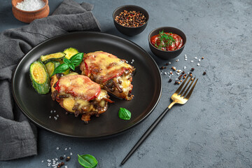 Meat with vegetables and cheese with a side dish of zucchini on a dark gray background.