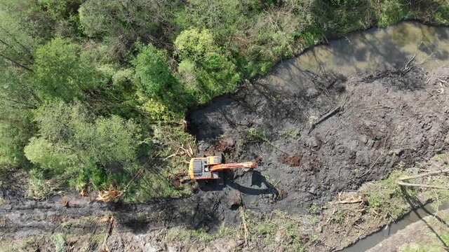 A crawler excavator fells trees and digs the ground. View from above. A bulldozer clears swamps to build new projects.