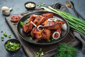 Fried meat, kebab, barbecue in a black plate on a dark gray background.