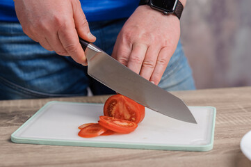 A man cuts a red tomato on a board. Healthy eating