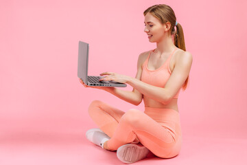 beautiful fitness woman using laptop over isolated pink background