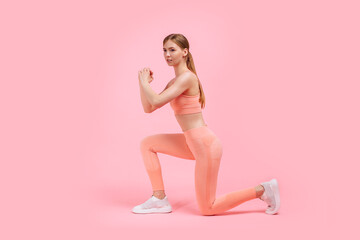 Fitness woman doing lunges exercises to train leg muscles, woman doing lunge exercise on one leg forward, on pink background