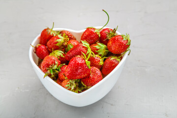 Fresh large strawberries in a white plate in the shape of a heart on the table.