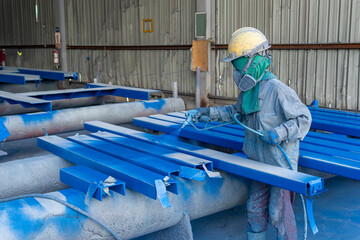 Painter is working to painting color top coat on steel structure with spray gun, at industrial factory.