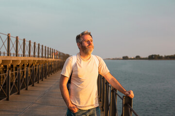 Fototapeta premium A young man is standing on the pier against the backdrop of the seascape and looking at the sunset. Huelva, Spain.