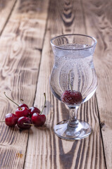 a glass of fresh sparkling water with a cherry on a wooden background. refreshing drinks in hot weather