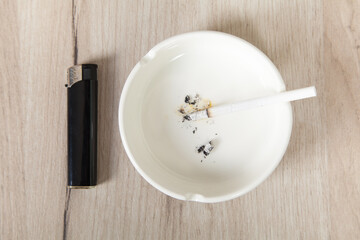 Ashtray, lighter, cigarette on a wooden background.