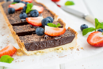 Chocolate cream tart with fresh blueberries and strawberries on top on a white wooden background. Summer dessert.