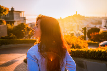 A young woman stands on a beautiful Lombard Street during sunset in San Francisco
