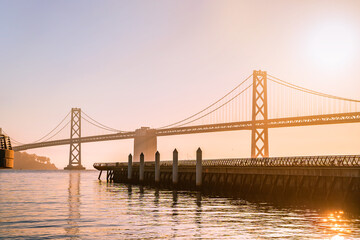 Incredible view of the Oakland Bay Bridge and the waterfront in San Francisco at sunrise, photographed from the pier - obrazy, fototapety, plakaty