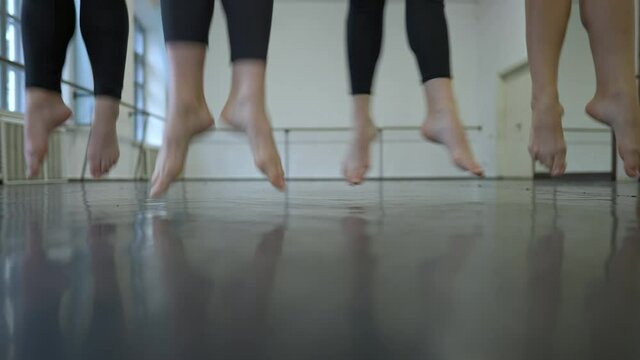 Legs of four unrecognizable ballet dancer jumping in third position in slow motion. Group of talented slim young Caucasian women rehearsing dance indoors in studio. Lifestyle and art concept