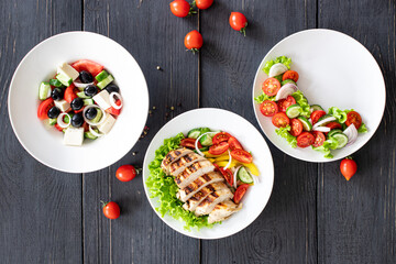 different salads vegetables, grilled chicken breast, olives, feta, tomato, onion, cucumber other on the table, healthy food