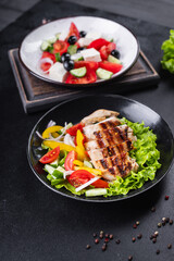 different salads vegetables, grilled chicken breast, olives, feta, tomato, onion, cucumber other on the table, healthy food