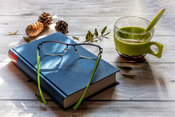 Book, glasses, glass on a worn white wooden table.