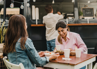 Mature women having fun eating at food truck outdoor - Focus on right face