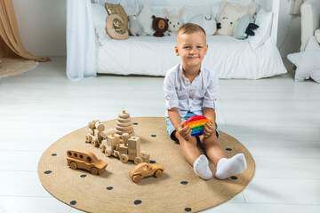 Portrait blonde boy with pop it sensory toy different forms. Boy presses colorful rainbow squishy soft silicone bubbles in children's playroom. Stress and anxiety relief. Trendy fidgeting game.